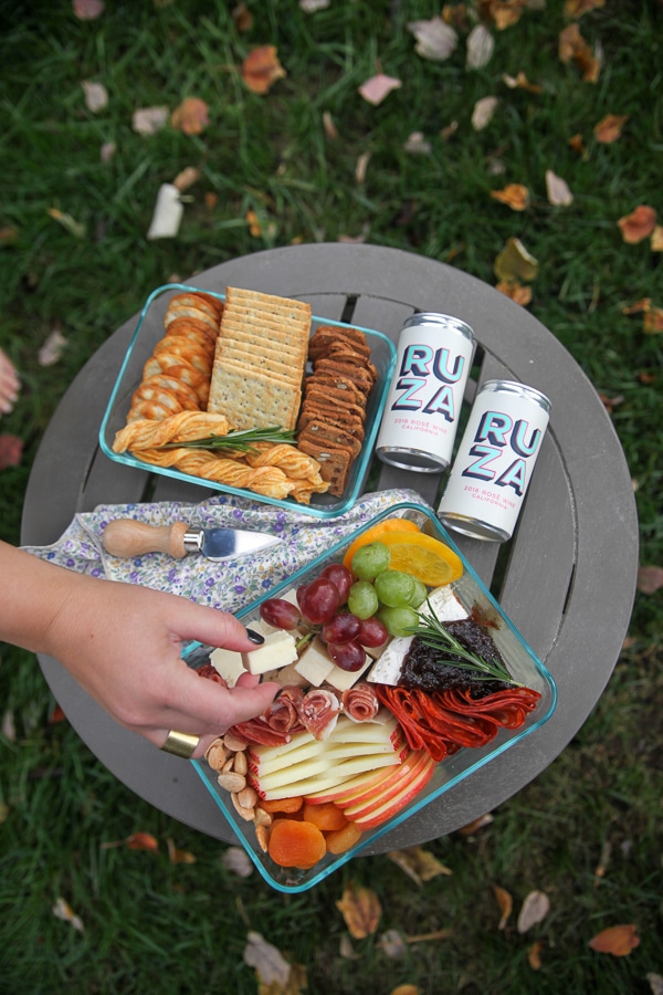 a hand taking cheese from a picnic cheese board