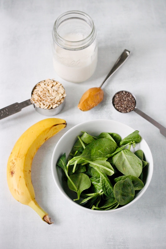 Overhead shot of measured smoothie ingredients: milk, oats, peanut butter, chia seeds, banana, and spinach. 