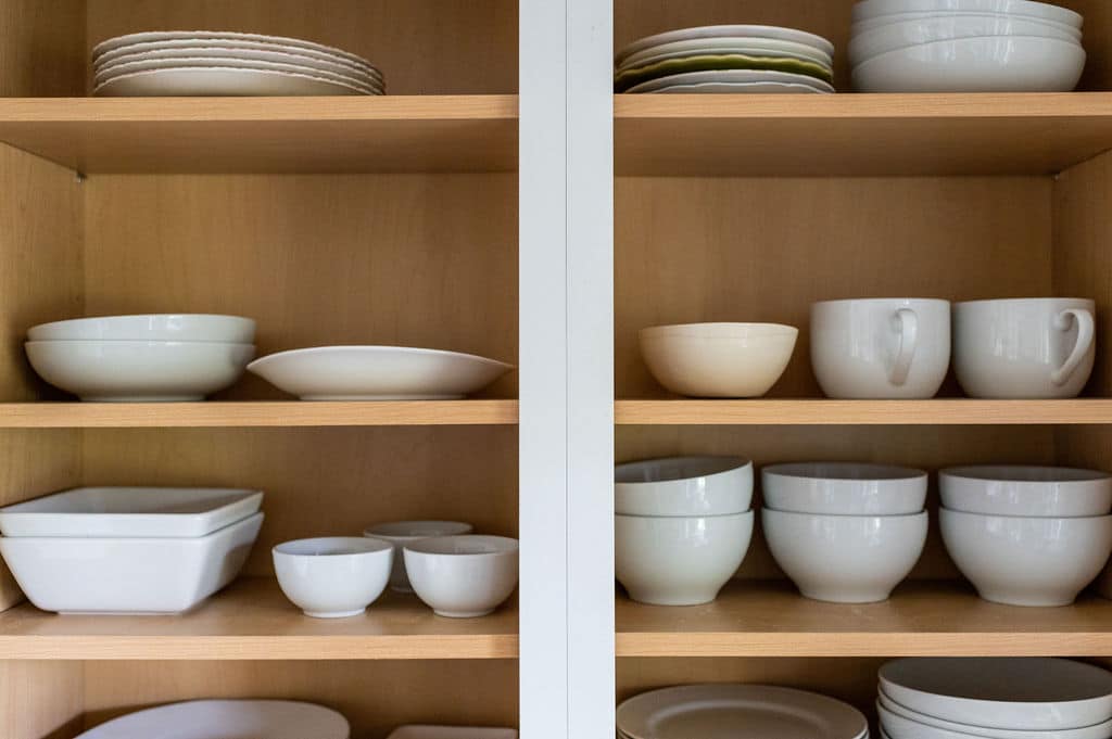 Organized white dishes in kitchen cabinet.