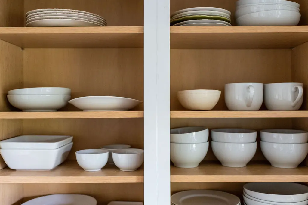 Organized white dishes in kitchen cabinet.