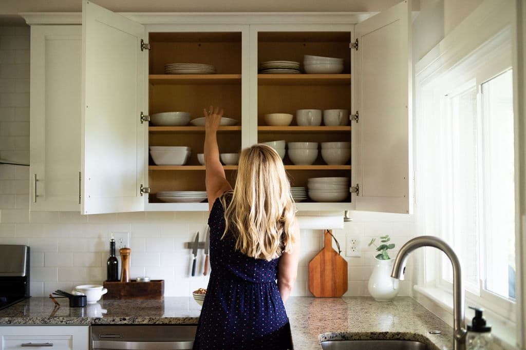 Kath Younger in kitchen grabbing a white dish from cabinet.
