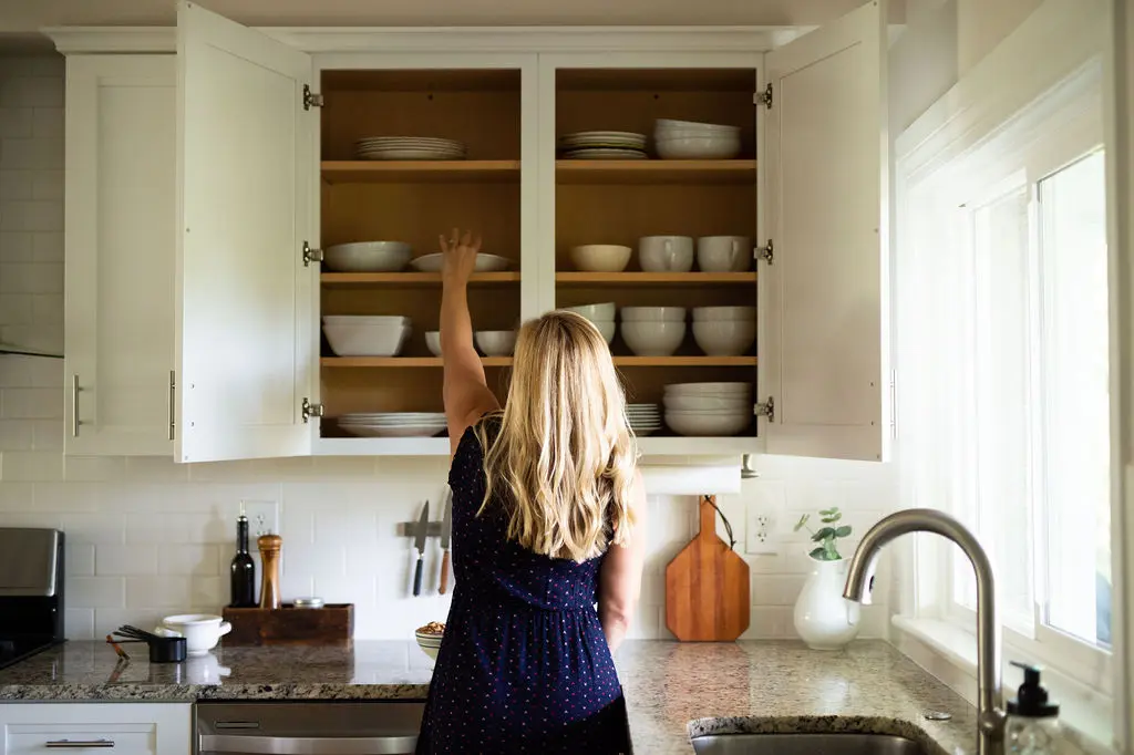 Kath Younger in kitchen grabbing a white dish from cabinet.