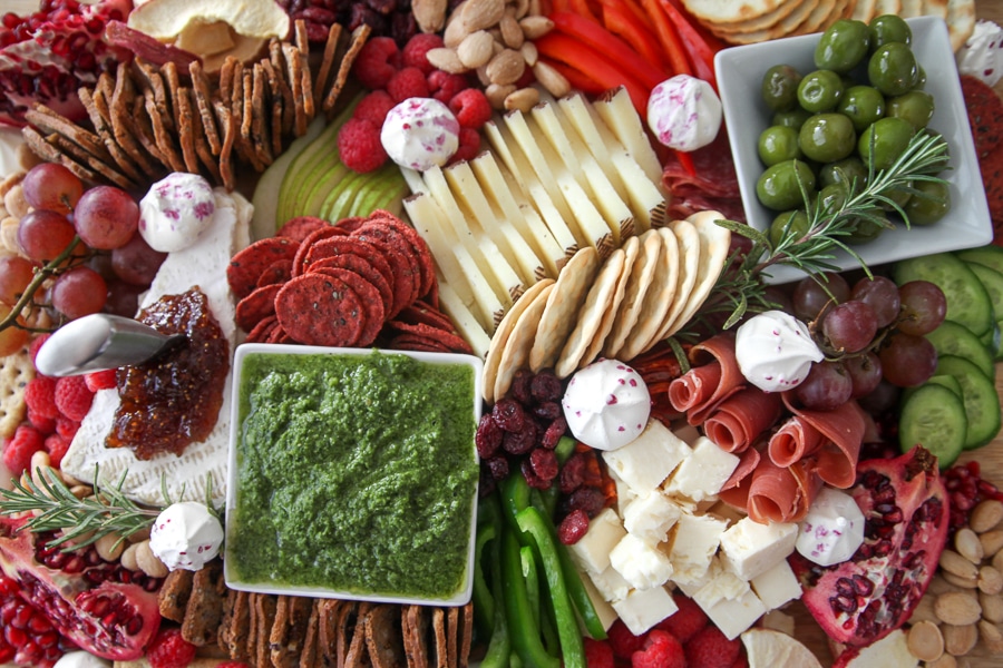 Overhead view of holiday grazing board: brie, cheddar, cured meats, grapes, dried fruit, crackers and rosemary sprigs