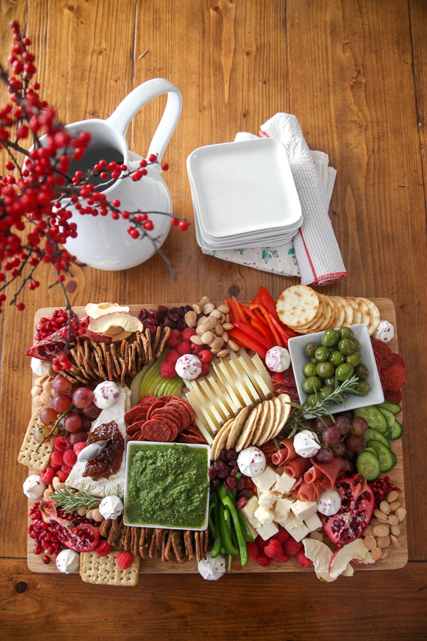 Red, white, and green Christmas charcuterie board with cheeses, fruits, crackers, nuts and festive garnishes on wood board on a dining table