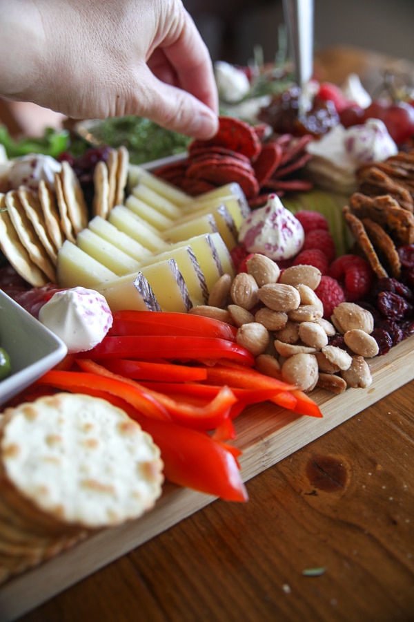 Slices of manchego and cheddar, rolled prosciutto, red bell peppers and almonds on a charcuterie board