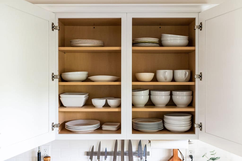 Open kitchen cupboards with white stacks of white plates and bowls.