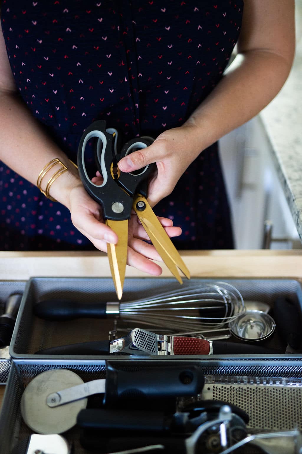 Hands holding set of gold scissors over open kitchen drawer. 