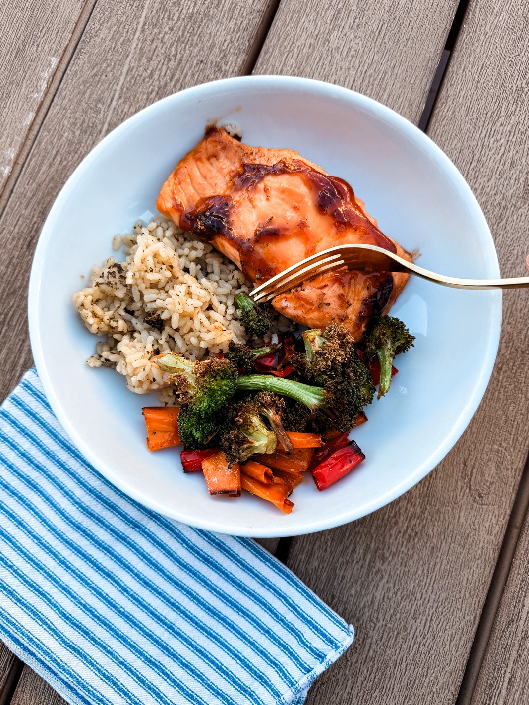 teriyaki salmon in a bowl with roasted broccoli, peppers, and rice being cut with a fork