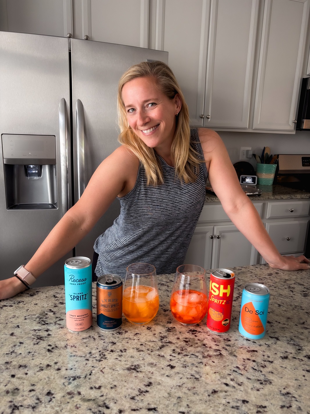 Kath in her kitchen with an array of nonalcoholic aperol spritzes on the counter 